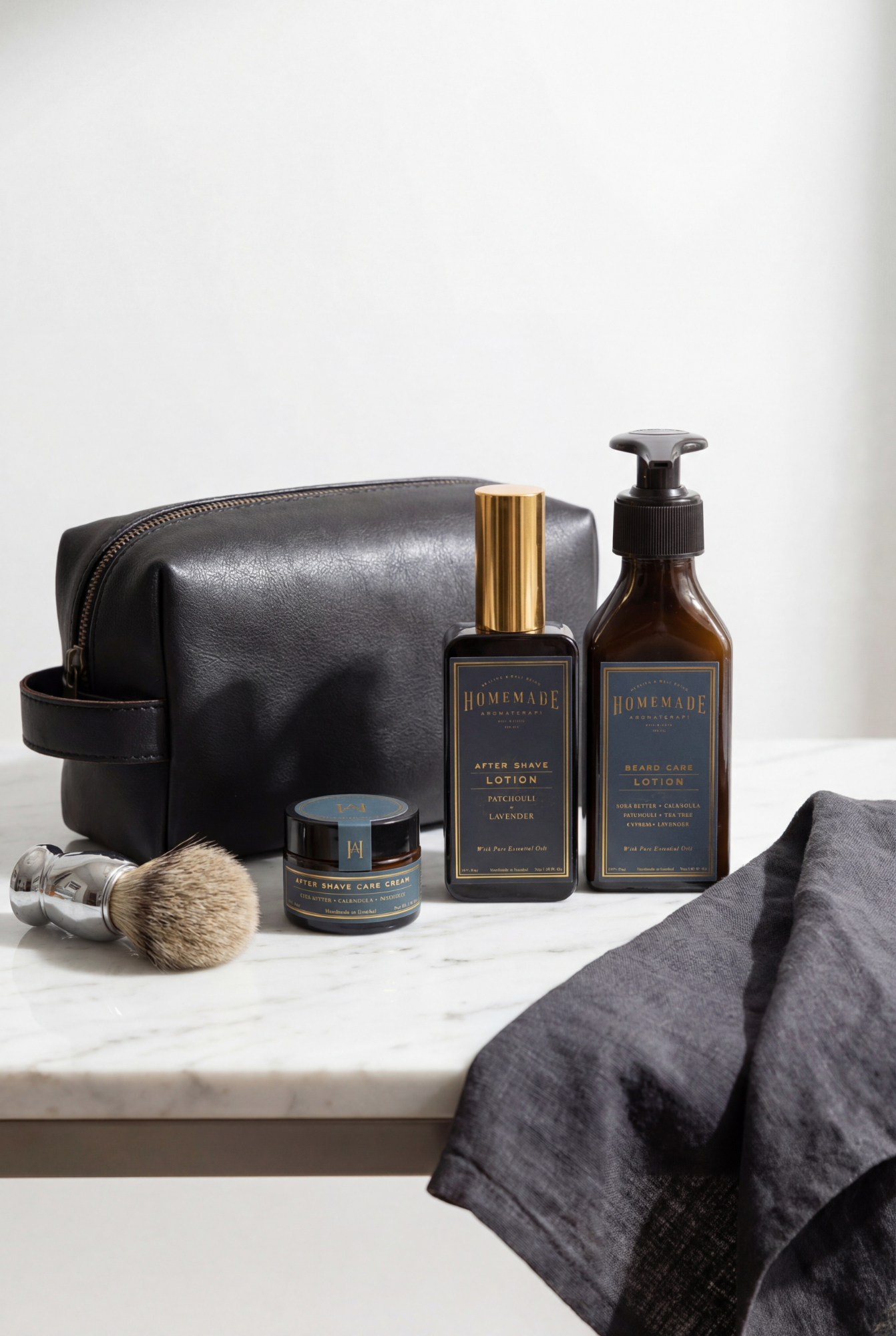 Homme Ritual men's grooming set with leather dopp bag, shaving brush, after shave cream, after shave lotion and beard care lotion on a marble surface.